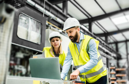 A portrait of an industrial man and woman engineer with laptop in a factory, working.