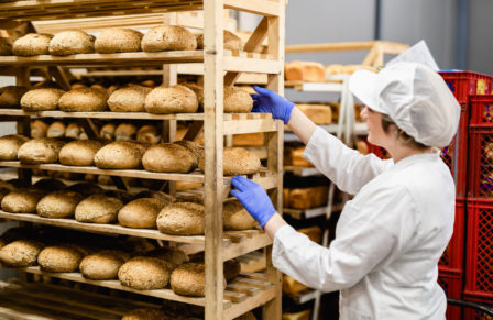 Young,Female,Worker,Working,In,Bakery.,She,Puts,Bread,On